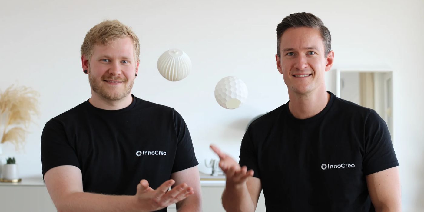 Lennart und Alex, die beiden Gründer von InnoCreo, sitzen in schwarzen InnoCreo-Shirts nebeneinander und werfen sich zwei 3D-gedruckte Lampenschirme zu
